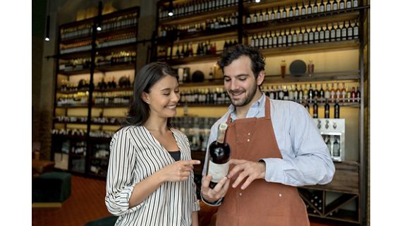 Beautiful Latin American woman at a cellar asking sommelier about a bottle of wine