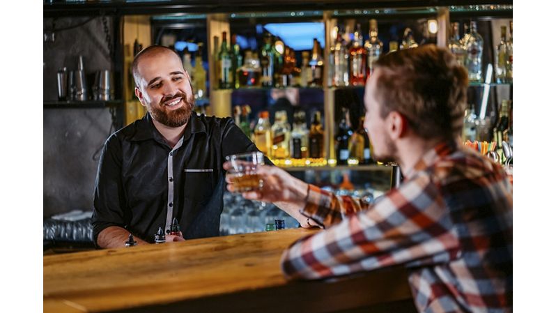 Young Caucasian Man drinking whiskey at bar counter and talking with bartender.
