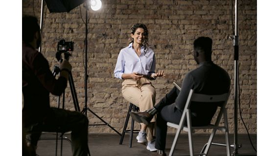 Happy attractive woman sitting on a bar stool and giving an interview to a male journalist in front of her, gesturing with her hands while she's talking and smiling