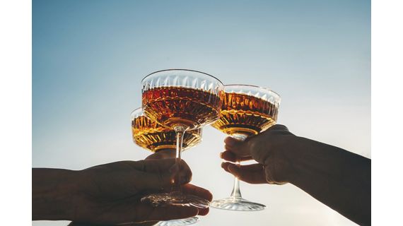 A close-up shot of friends clinking sparkling wine glasses at sunset. Refreshing cocktail drinks. Summer outdoor parties and celebrations concepts