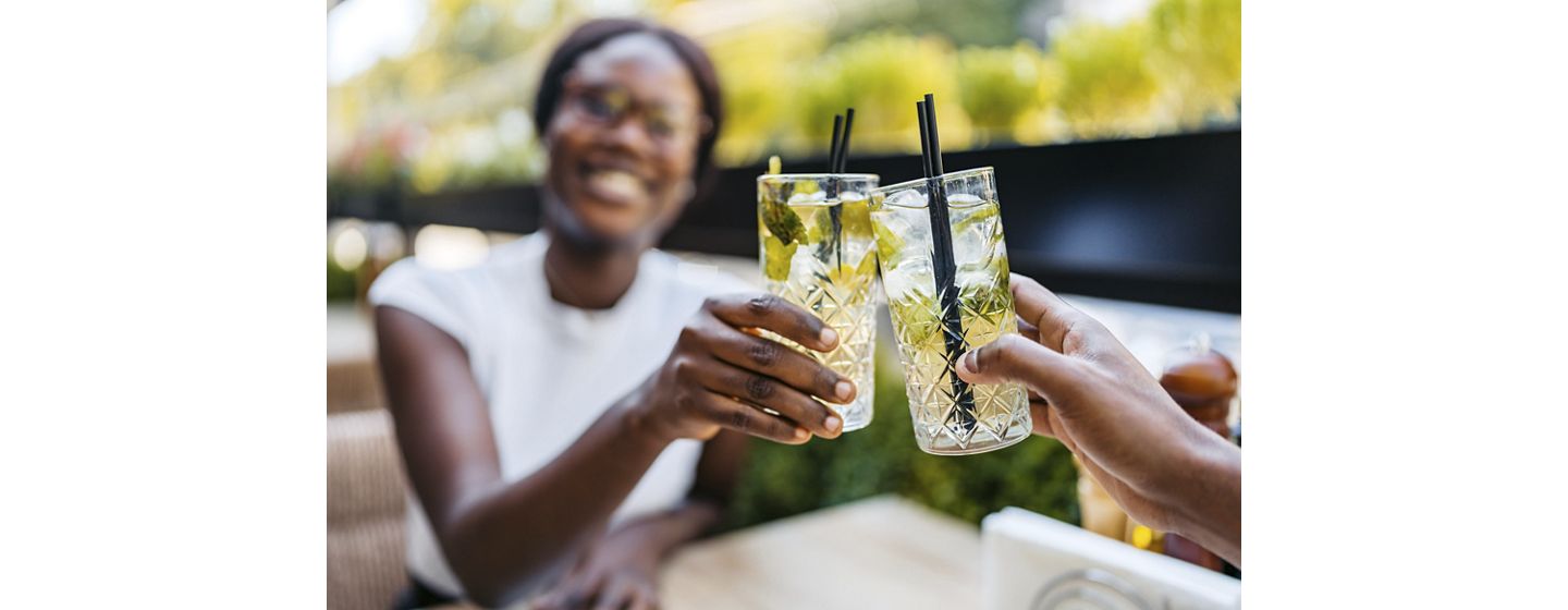 Beautiful young black couple drinking mojito cocktails in a bar outdoors. Having a celebratory toast.