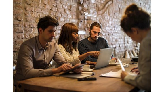 Group of multi-tasking business people working in the office. Focus is on African American woman showing something on laptop to her male colleagues.