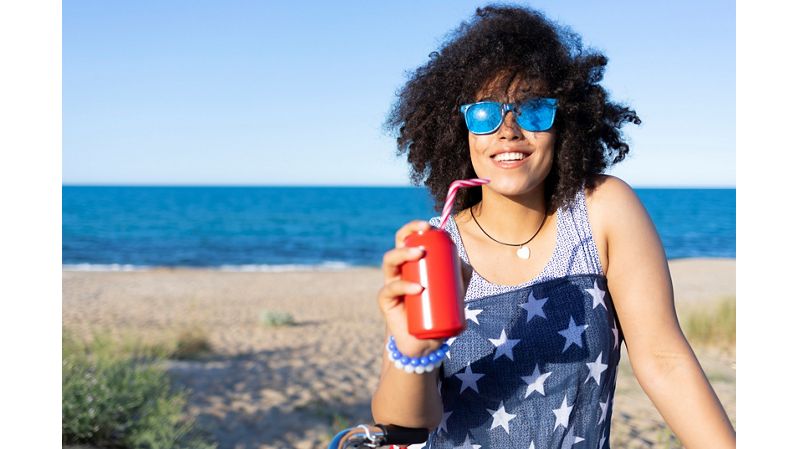 Woman at the beach drinking a canned beverage with a straw