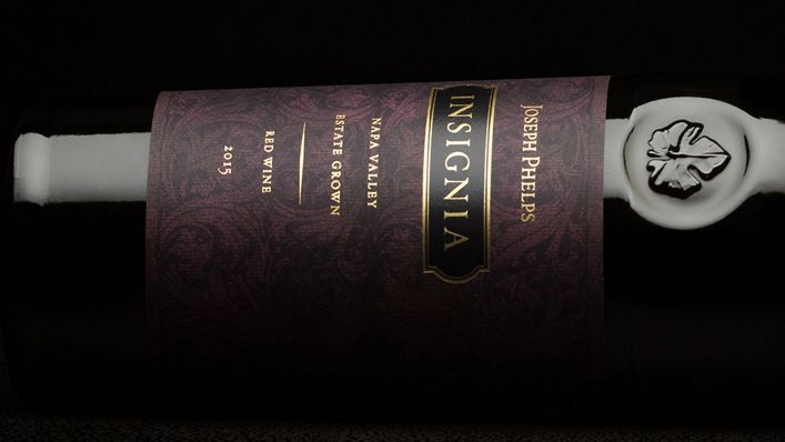 A close-up of a Joseph Phelps Vineyards Insignia wine bottle on its side, highlighting the intricate label design and wax-sealed neck against a dark background.