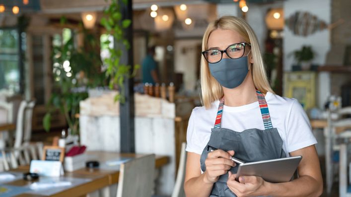 Portrait of a beautiful happy waitress working at a restaurant wearing a facemask during the COVID-19 pandemic Ã¢Â Â  food service concepts