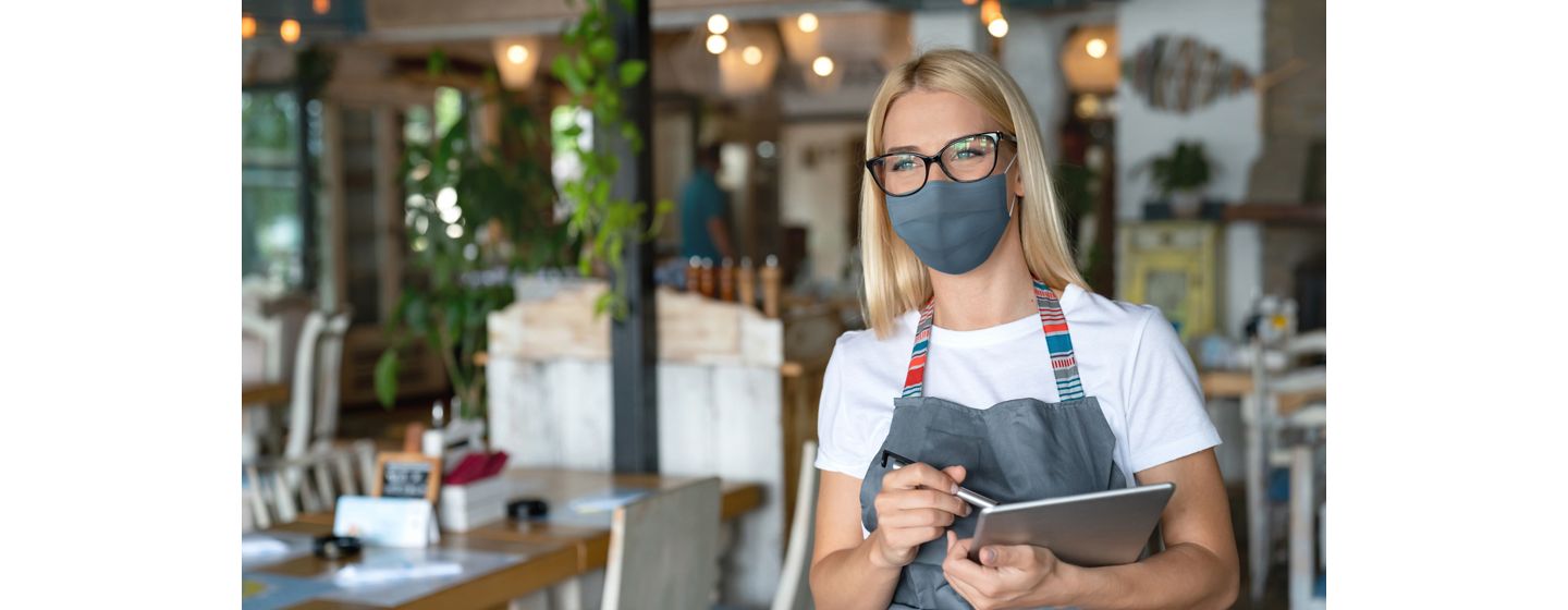 Woman wearing mask holding a tablet in a restaurant.