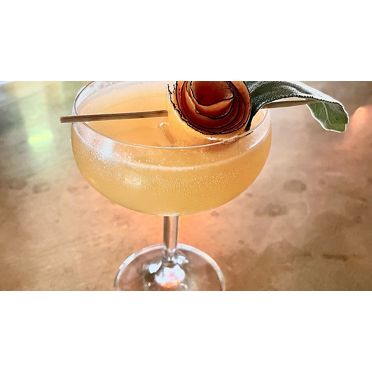 A fizzy Femme Brulee cocktail, focusing on its artistic apple garnish.