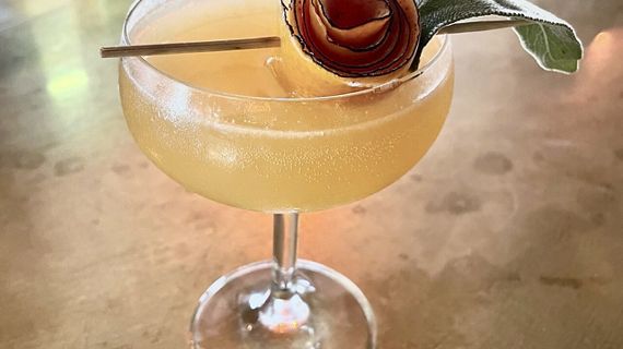 A close up of a fizzy Femme Brulee cocktail, focusing on its artistic apple garnish.