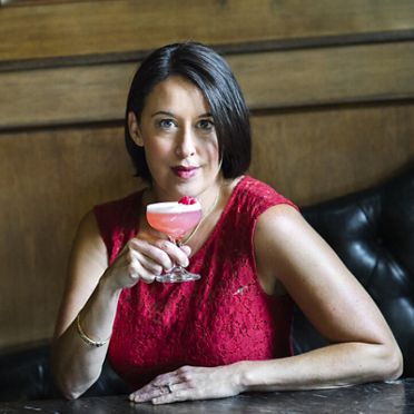 A woman in a red dress, confidently holding a pink cocktail.