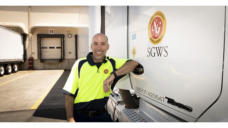 A smiling man in a neon yellow and black uniform leans on a Southern Glazer's Wine & Spirits delivery truck, exuding a friendly, professional demeanor.