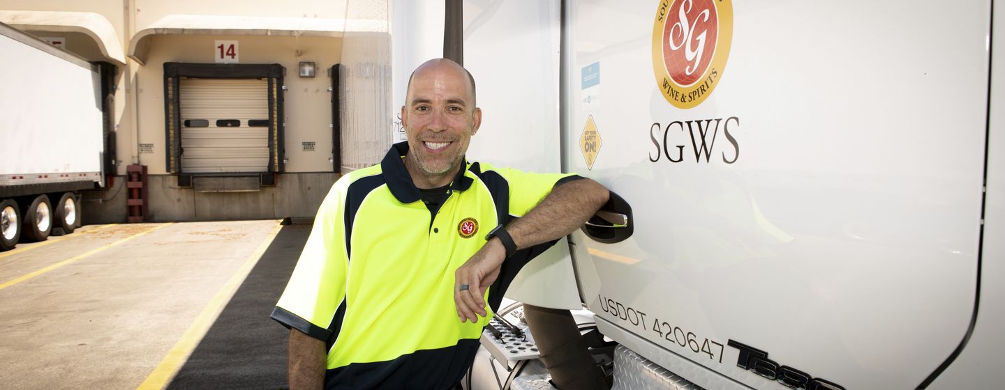 A smiling man in a neon yellow and black uniform leans on a Southern Glazer's Wine & Spirits delivery truck, exuding a friendly, professional demeanor.