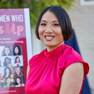 Sheena Yap Chan, author of Women Who Step Up, posing confidently in front of a banner for her book with a bright smile.