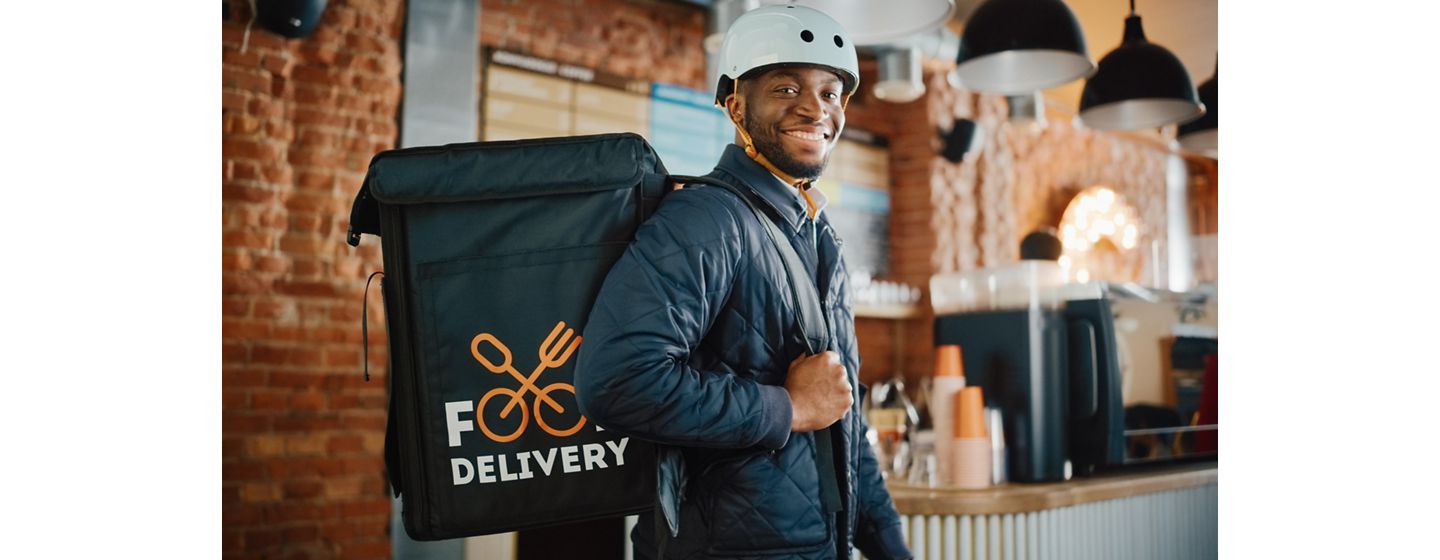 Man with a helmet holding a large food delivery backpack over his shoulder