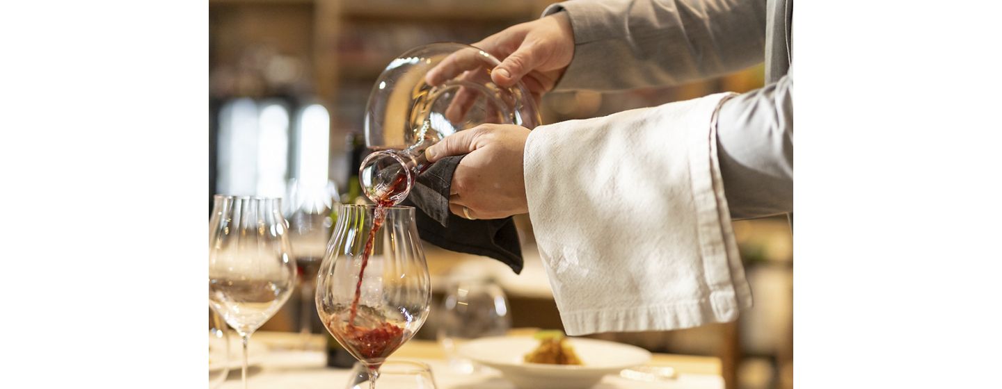 Close-up shot of unrecognizable waiter pouring red wine into wine glass in a luxurious hotel restaurant