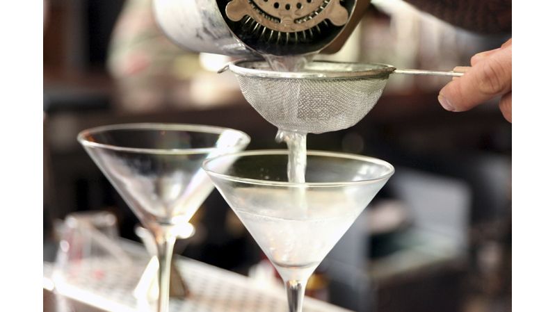 a bartender pouring martinis into chilled glasses through a small wire mesh strainer.