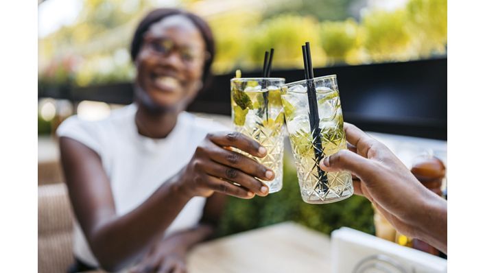 Beautiful young black couple drinking mojito cocktails in a bar outdoors. Having a celebratory toast.