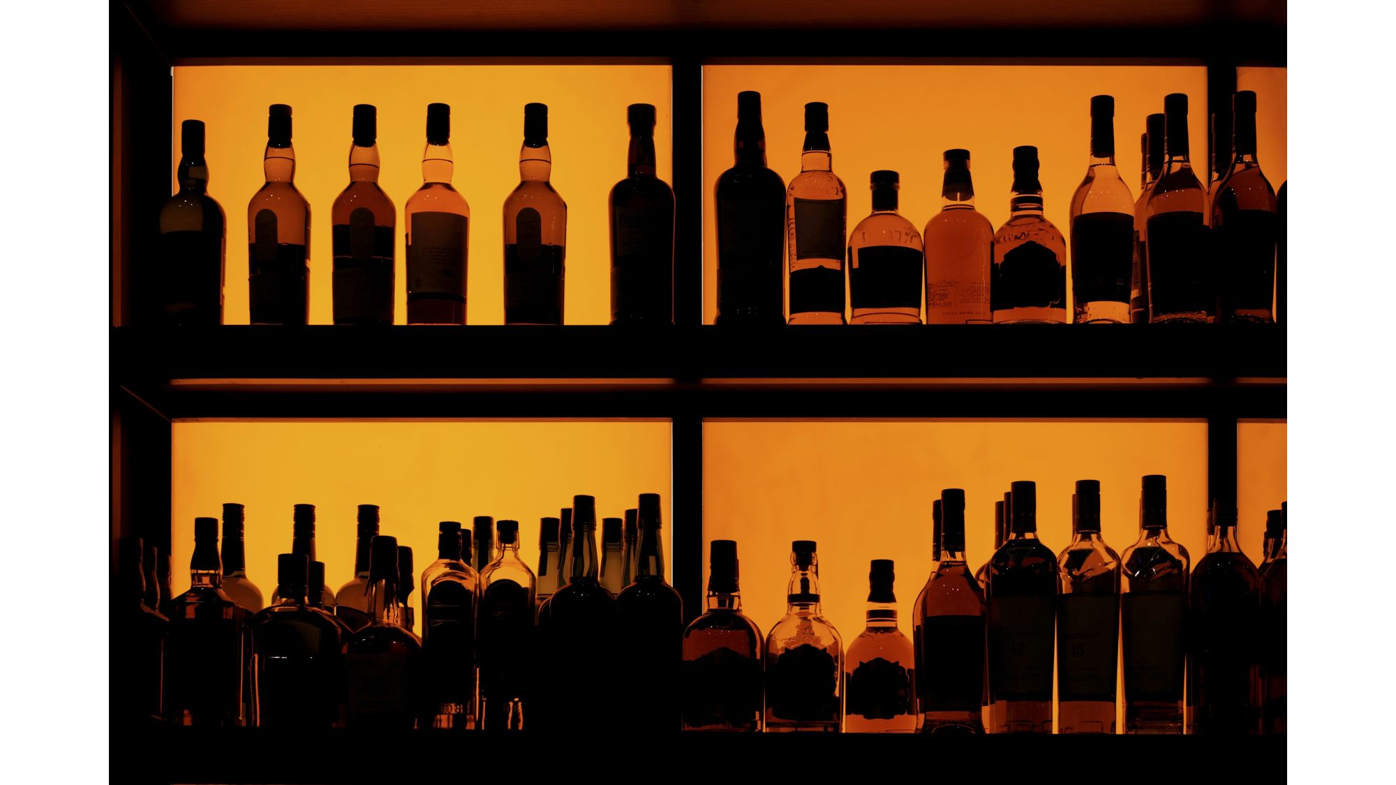 Bottles sitting on shelf in a bar, back lit